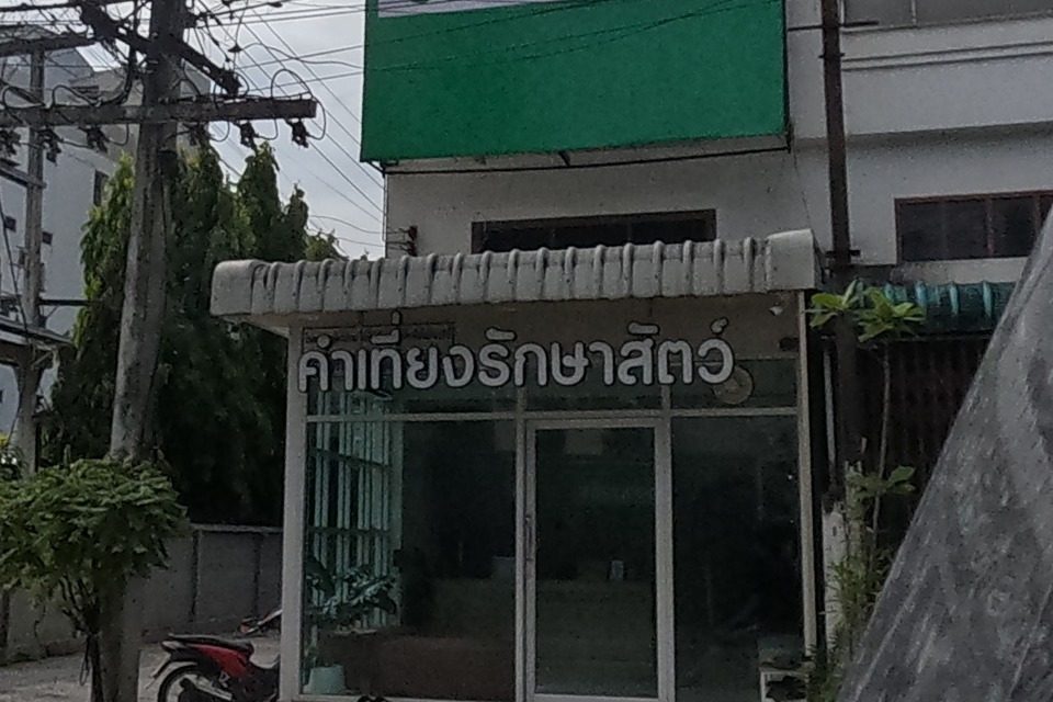 'โรงพยาบาลสัตว์คำเที่ยง' (Kham Thiang Animal Hospital) is marked by a large green sign with two phone numbers over its glass-fronted clinic 'คำเที่ยงรักษาสัตว์', a scooter parked outside.