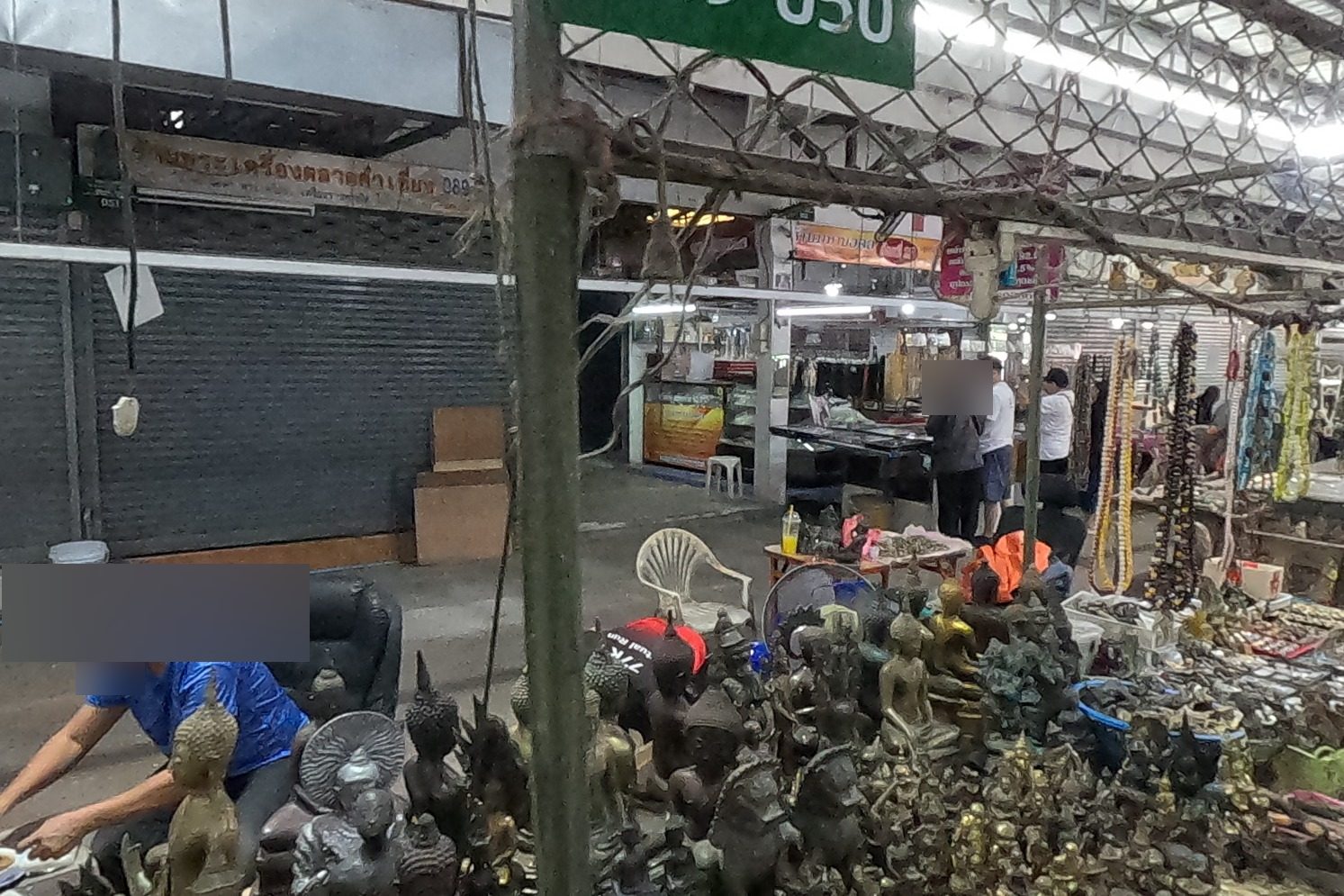 The วิไลพระเครื่อง lock plate over a stall packed with bronze Buddha images; a man in blue sets them out.