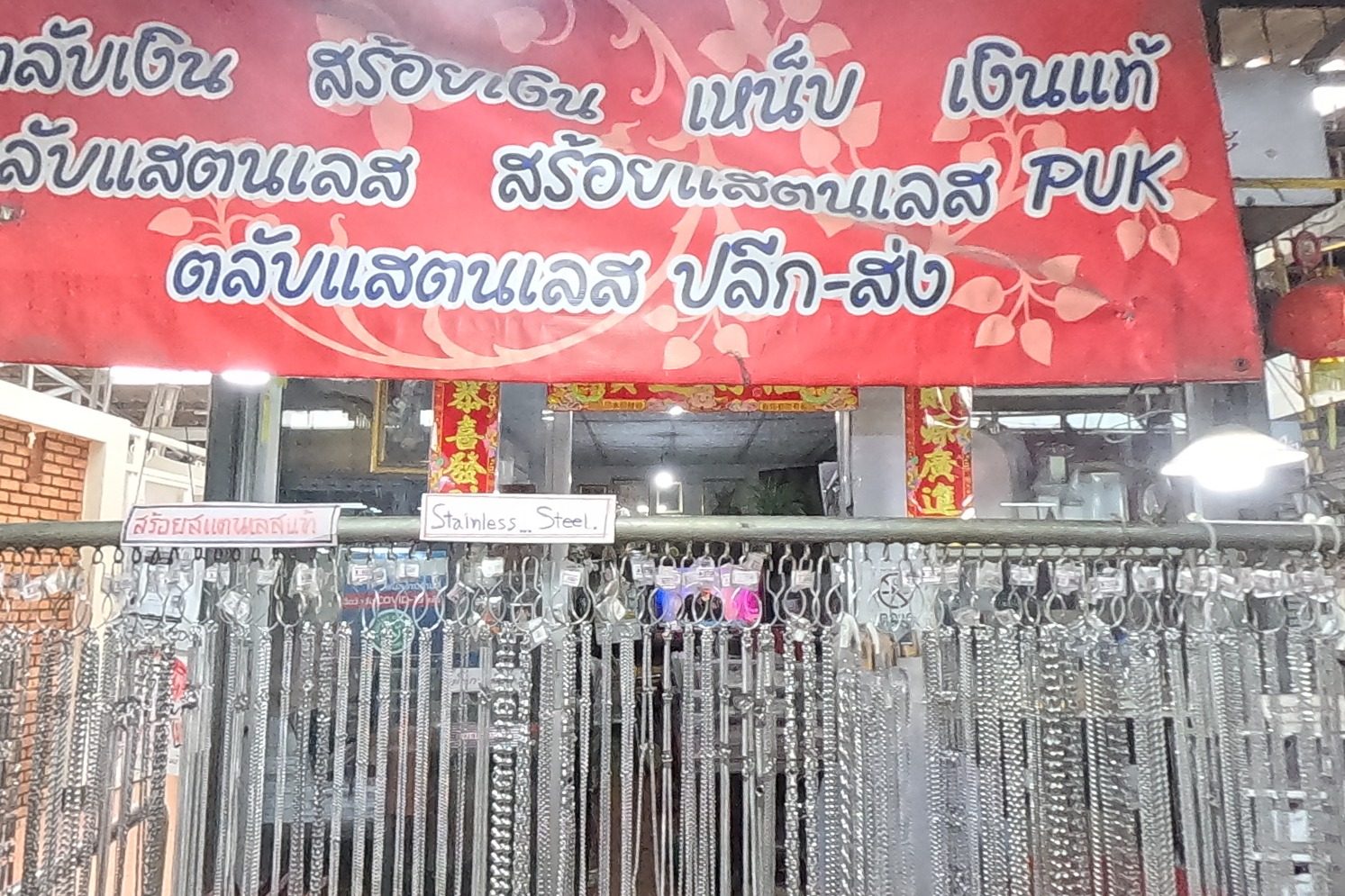 The PUK banner over racks of stainless and silver chains, with trays of gold-coloured amulet cases, pins and packets below.
