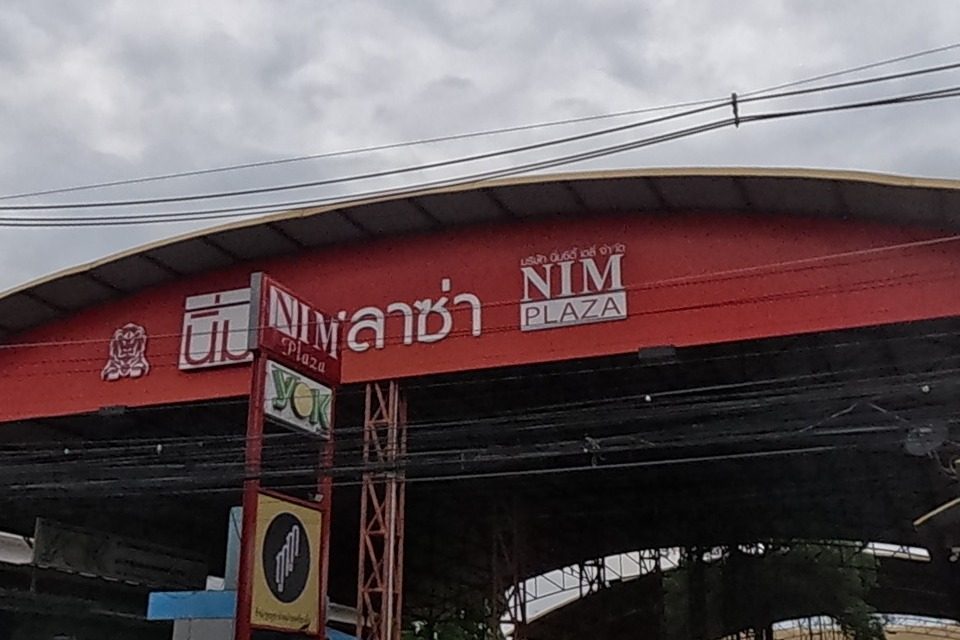 Nim Plaza, a covered market complex under a curved red roof, cars parked outside.