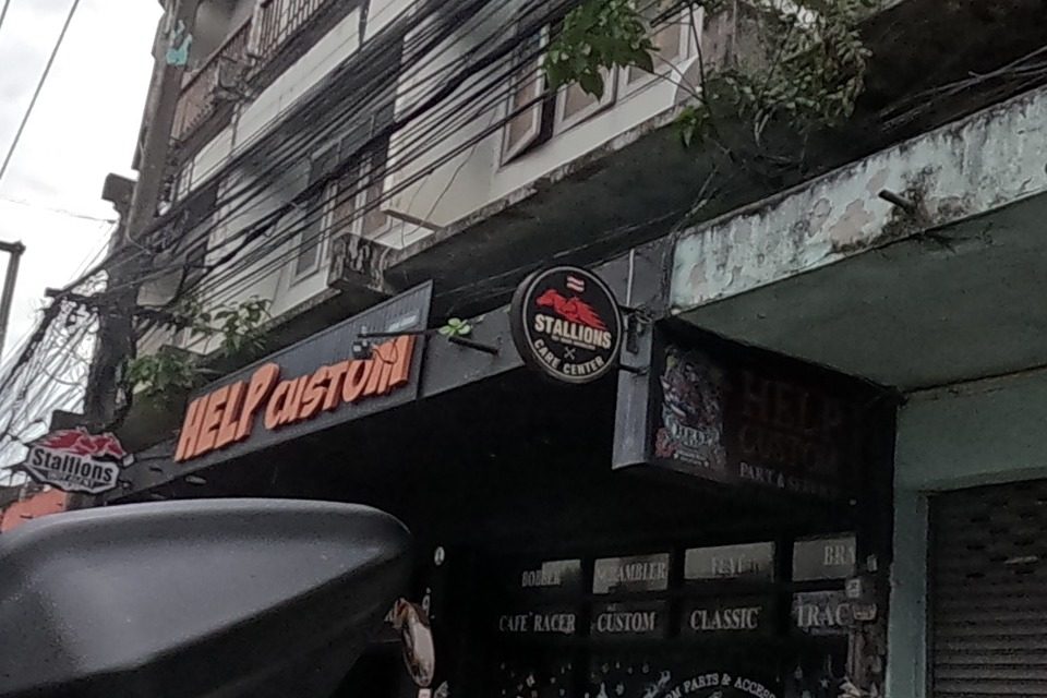 Chiang Mai Help Custom, a motorcycle customisation shop (bobber, scrambler, cafe racer, classic, tracker parts and accessories) next to Stallions Cafe Center, and Liver Pian Shop showing rows of black Harley-Davidson-style motorcycles inside a showroom.