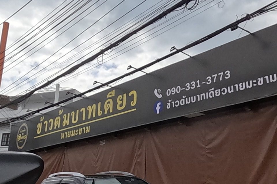 Khao Tom Baht Diao Nai Makham, a rice-porridge restaurant with its shutters down, phone 090-331-3773, a Coca-Cola fridge and a handsome gold-and-white spirit house on a naga-carved pedestal next door.