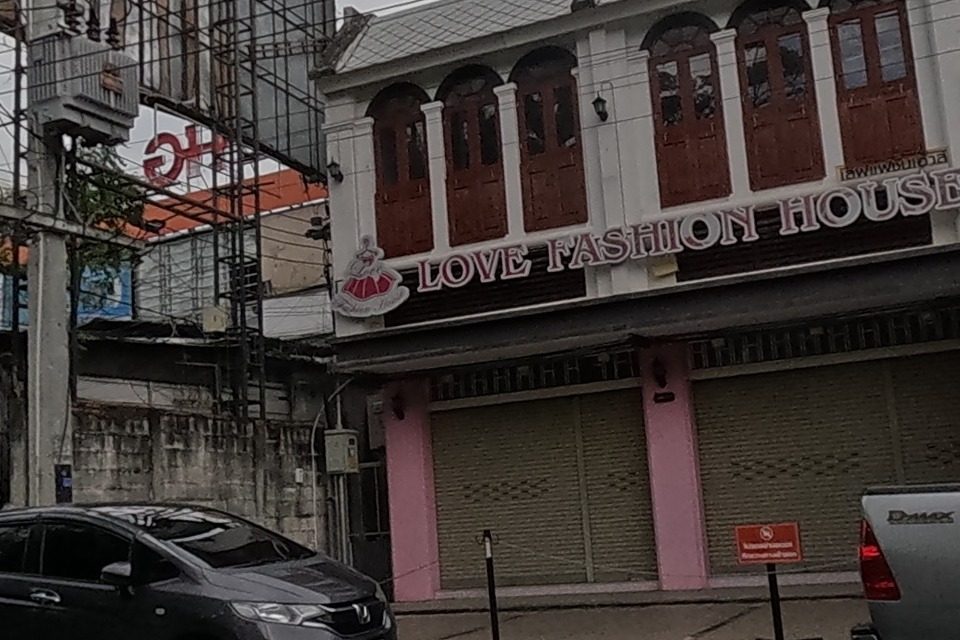 'Love Fashion House' occupies a colonial-style shophouse with arched windows, next to a CCTV/camera shop, a computer shop signed 'SPEED' / 'Chat & Shop' with Intel and AMD branding, and a 'เมืองไทย แคปปิตอล' loan-shop branch advertising 0.66% loans.