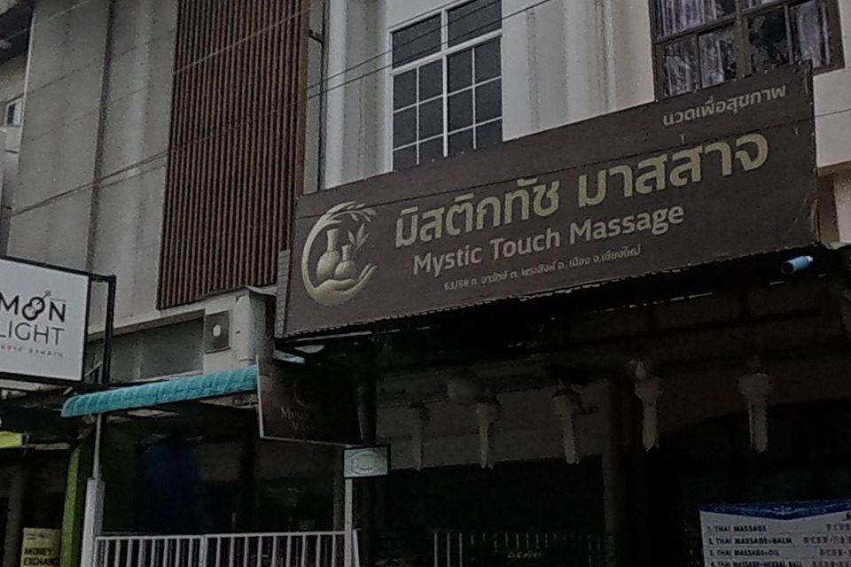 A massage shop with a wood-panel sign, and next door a street-food stall with an umbrella outside a pink-lit shop.
