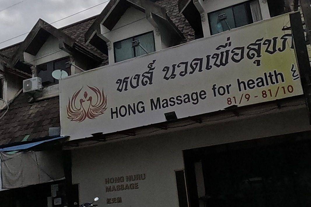 A two-storey shophouse with a large banner for Hong massage, and 'Hong Nuru Massage' lettered on the wall below; a teal building with a courtyard stands opposite.