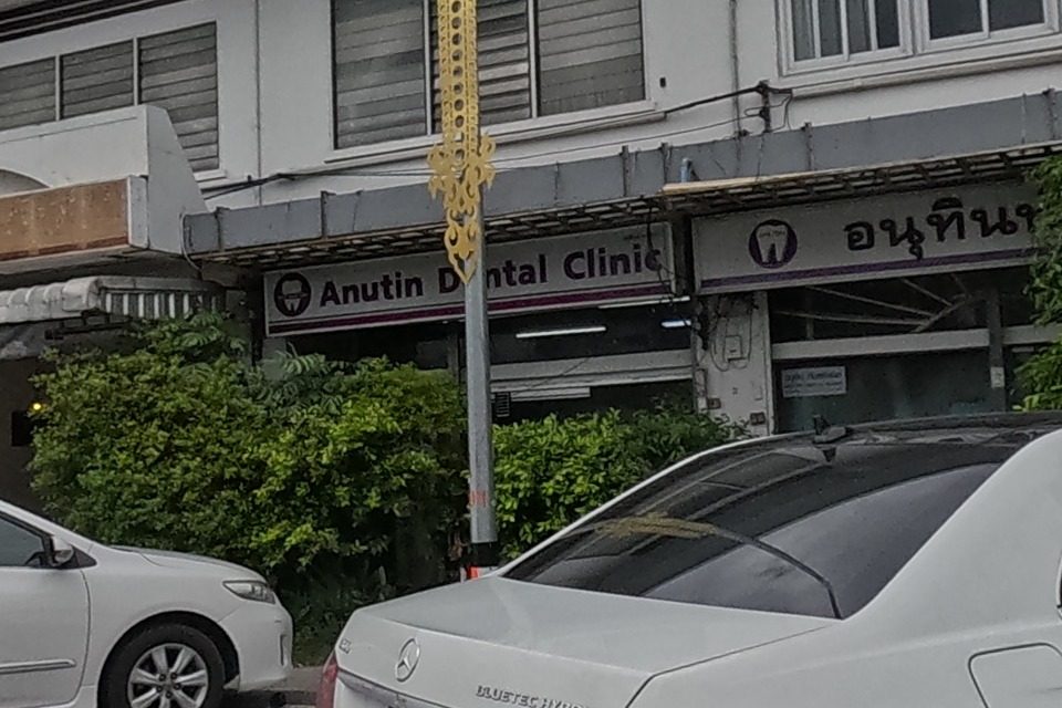 A dental clinic with English and Thai signage, next to a red shuttered shop.