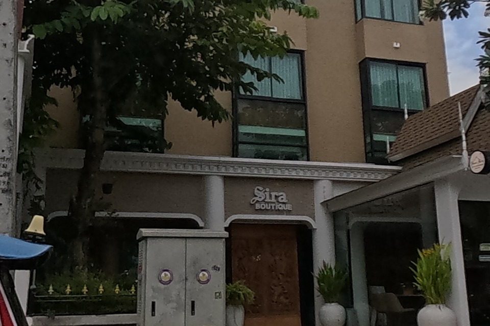 A red tuk-tuk passes an ornate patterned building and a boutique hotel signed 'Sira'.
