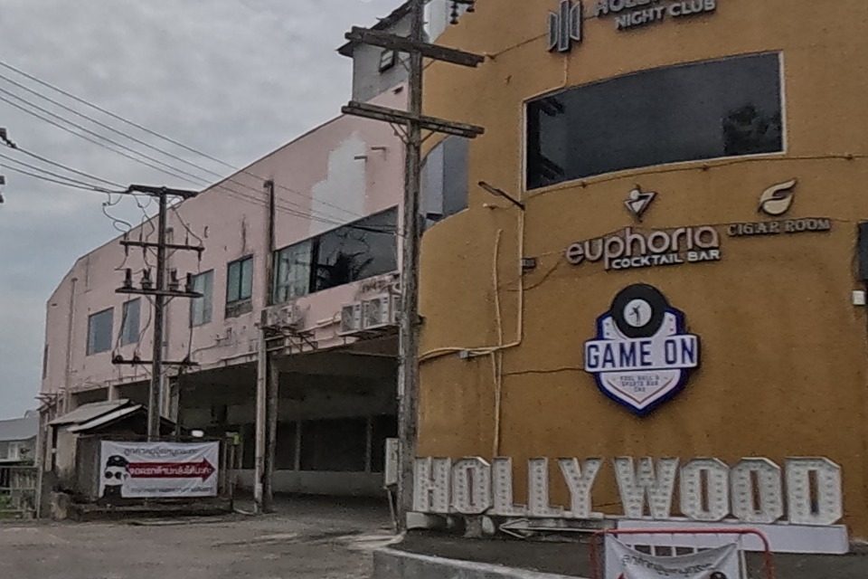A graffiti-covered remnant of the old city wall with a 'do not walk on ancient wall' sign, facing a yellow nightclub complex lettered 'HOLLYWOOD'.