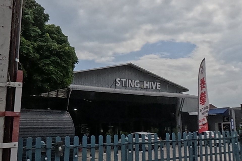 A muay thai gym's warehouse-style building named on its gable, behind a blue picket fence.