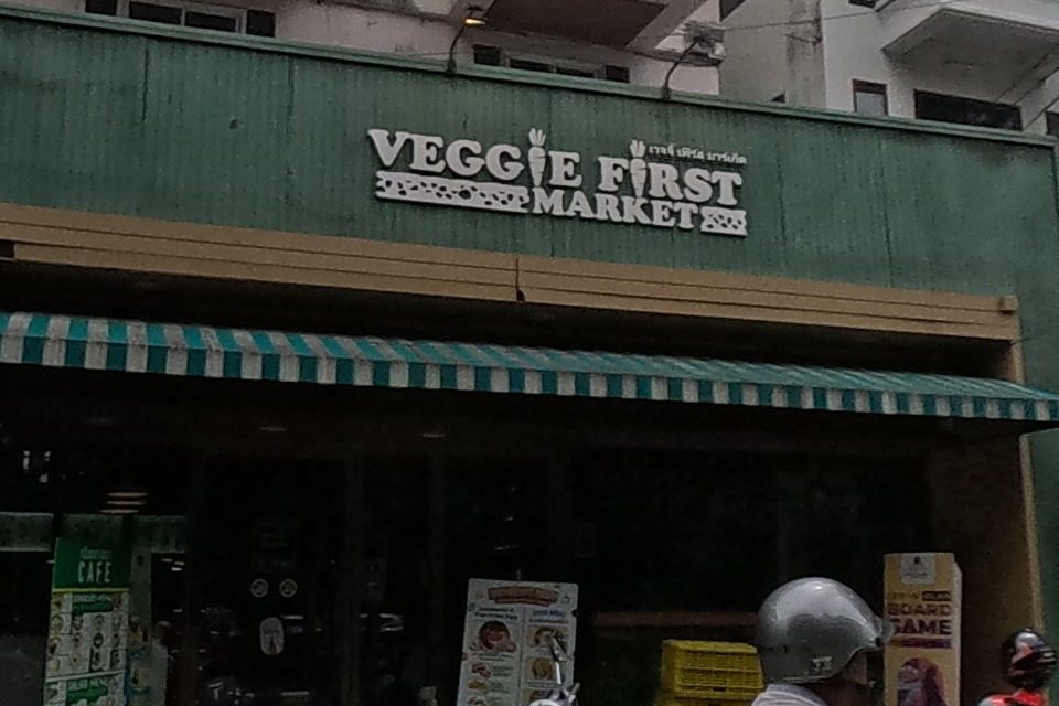 A green-fronted vegetarian grocery store, its neighbour shuttered and tagged with graffiti.
