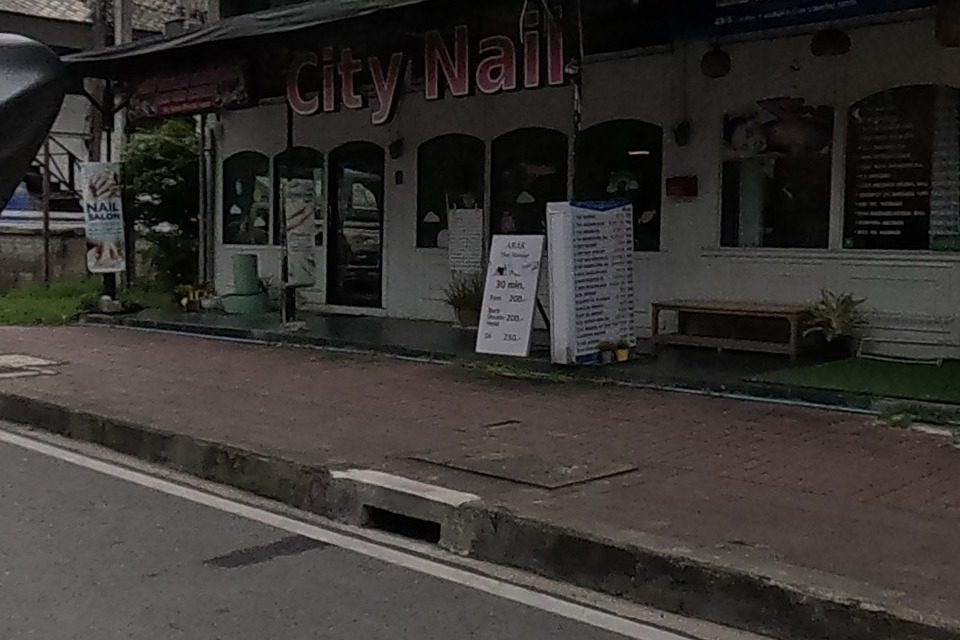 A ground-floor row holds a nail salon with a price board, a cafe with a yellow-striped awning and a soft-serve sign, and a hotel with a red banner.