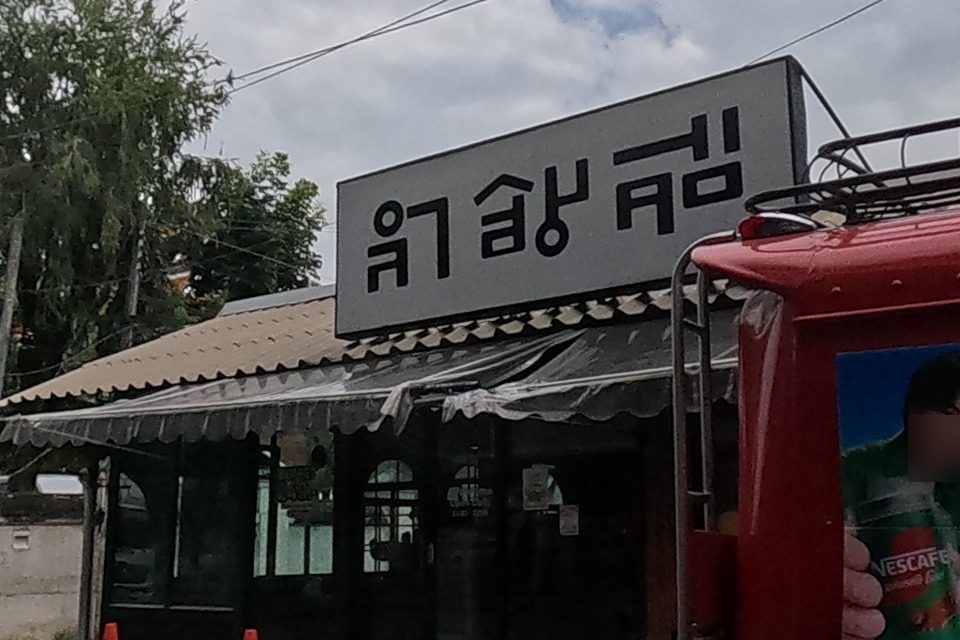 A red shared-taxi van with a Nescafe ad is parked outside a restaurant with a black-and-white sign.