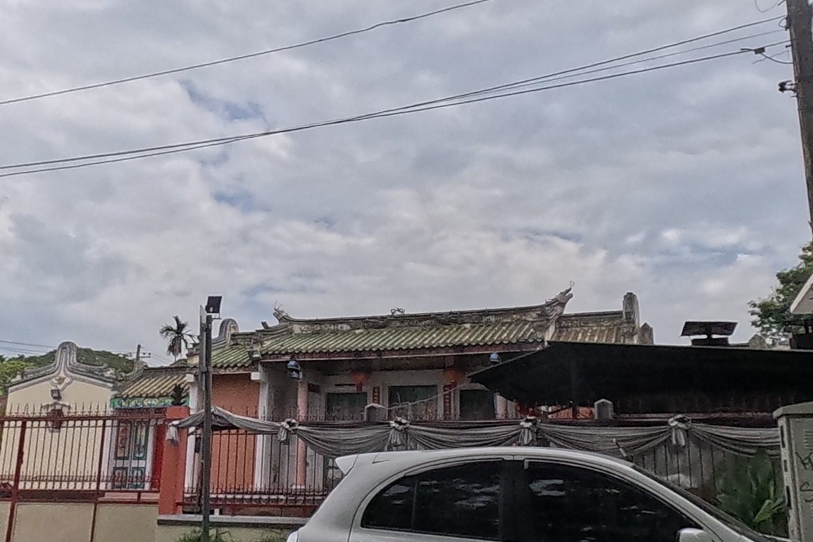 An ornate Chinese-style association hall with a dragon-ridge tiled roof sits behind a red iron gate, draped with white ceremonial cloth.