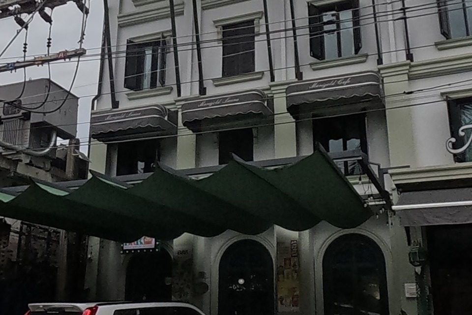 An ornate white hotel building with arched windows and a green awning sits behind parked cars.