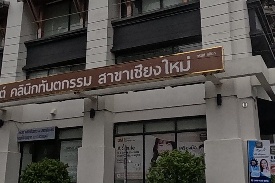 A dental and medical clinic occupies a white corner building, with a red 'for sale/rent' banner on a building across the intersection and a temple-mural utility box on the pavement.