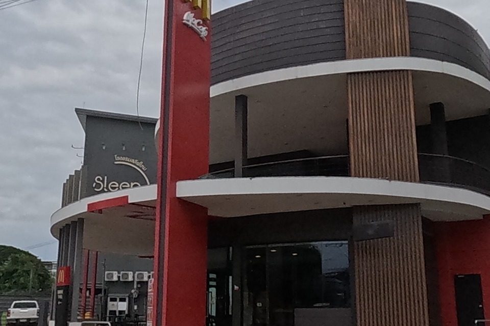 A curved red-and-white McDonald's building with golden arches sits at the corner, a tall red pylon sign beside it and a blue billboard behind.