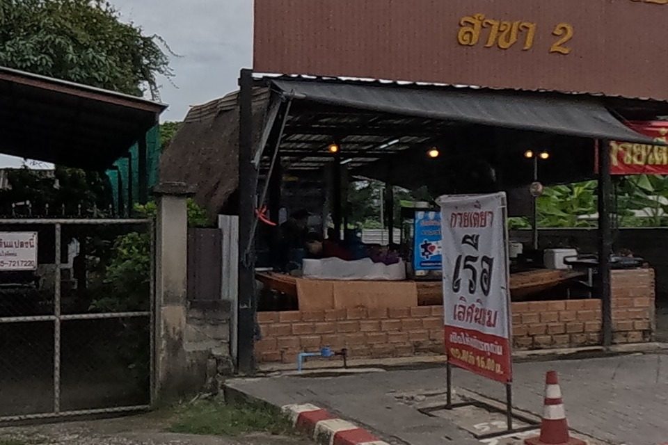 A boat-noodle restaurant, 'ก๋วยเตี๋ยวเรือเลิศนิยม สาขา 2', under an open-sided roof next to a gated house (No. 317/319); a red price banner reads noodles from 16 baht.