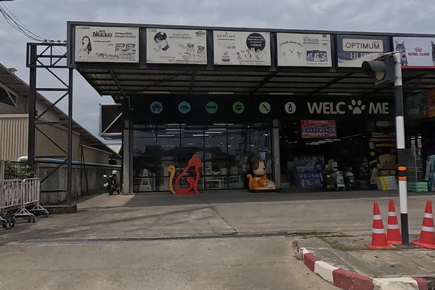 A pet-supply superstore with a 'WELCOME' entrance, mascot statues of a cat and dog out front, brand banners for pet food overhead.
