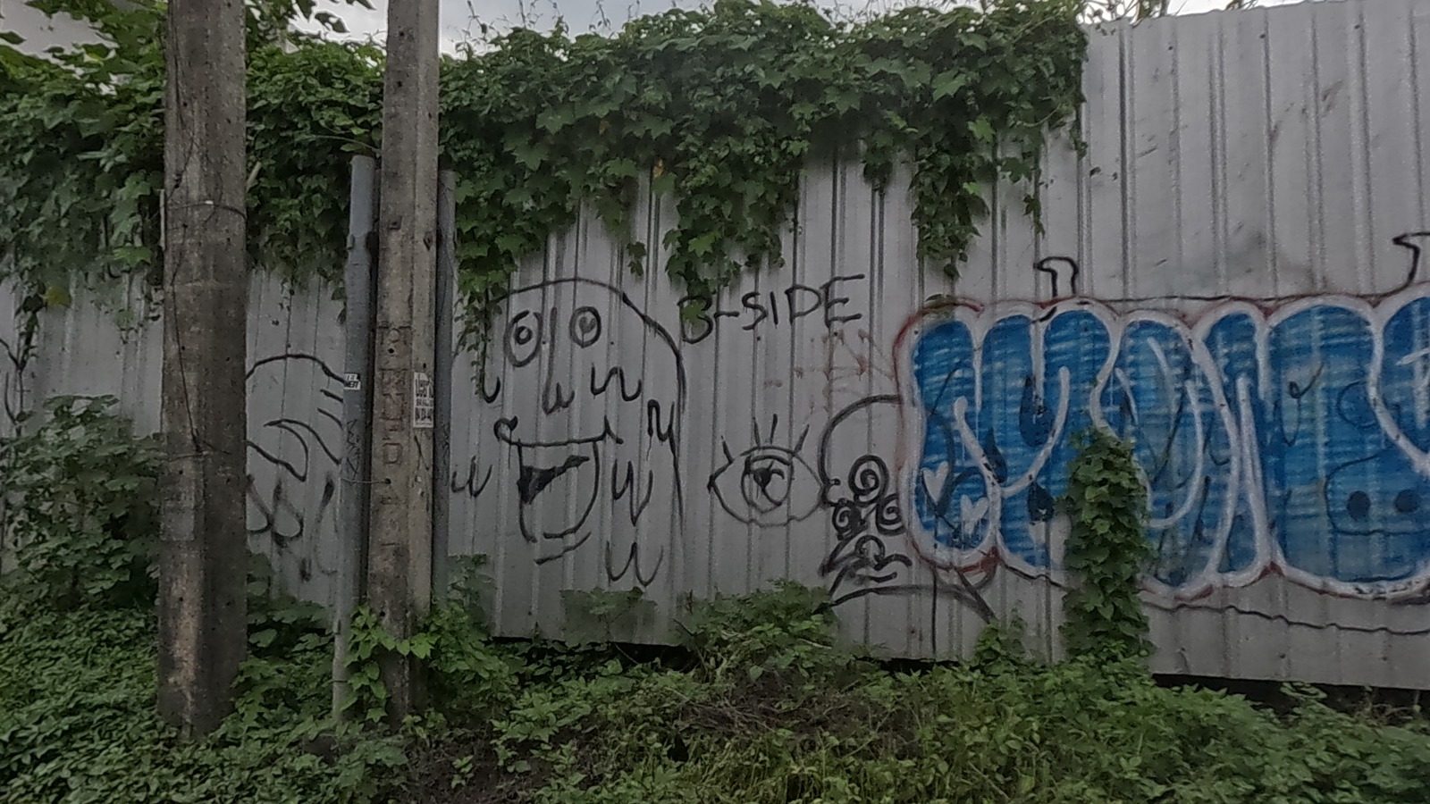 Cartoon face doodles and a blue bubble tag on a corrugated fence