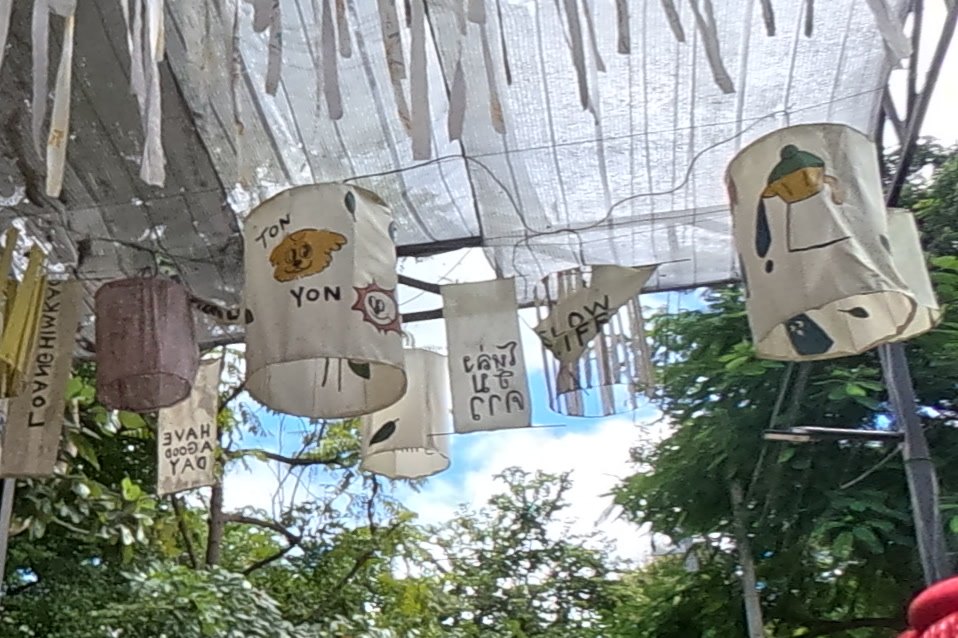 Painted cloth lanterns in the ribbon canopy — Chamcha Market, San Kamphaeng