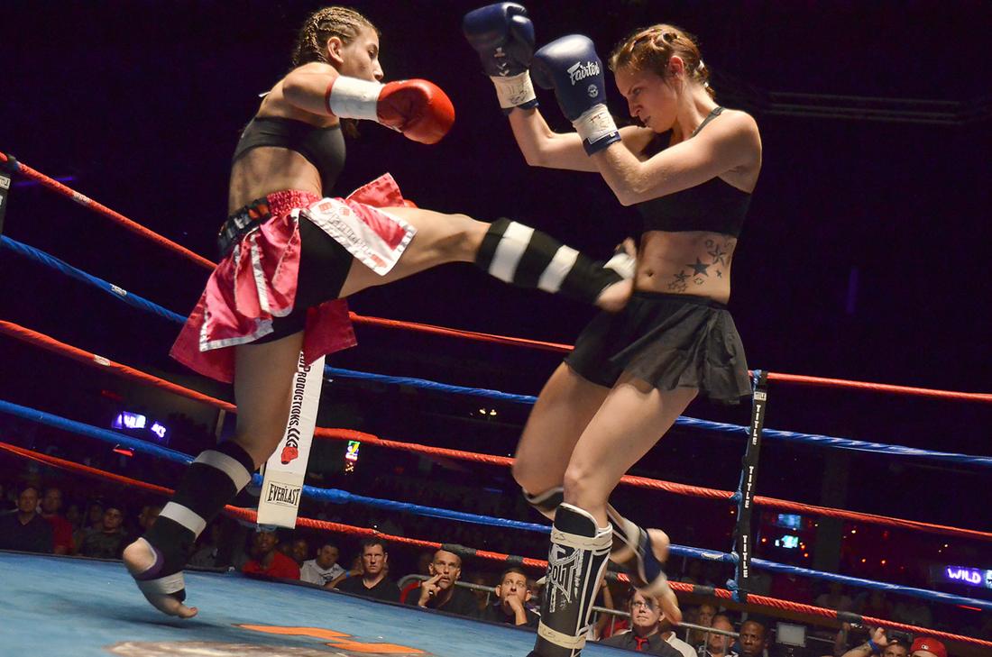 One fighter executes a Muay Thai teep kick against her opponent in a women's Muay Thai match.