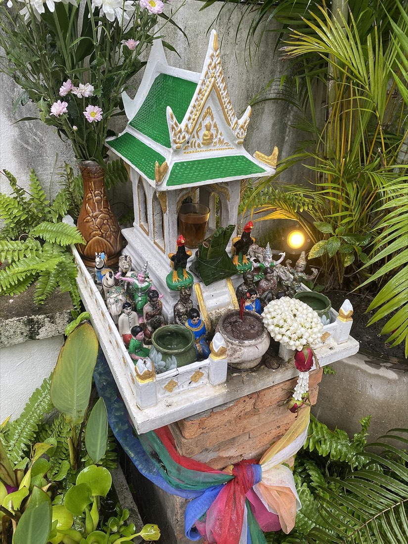 ศาลพระภูมิ ล้อมด้วยตุ๊กตาและพวงมาลัย · a spirit house crowded with figurines and garlands