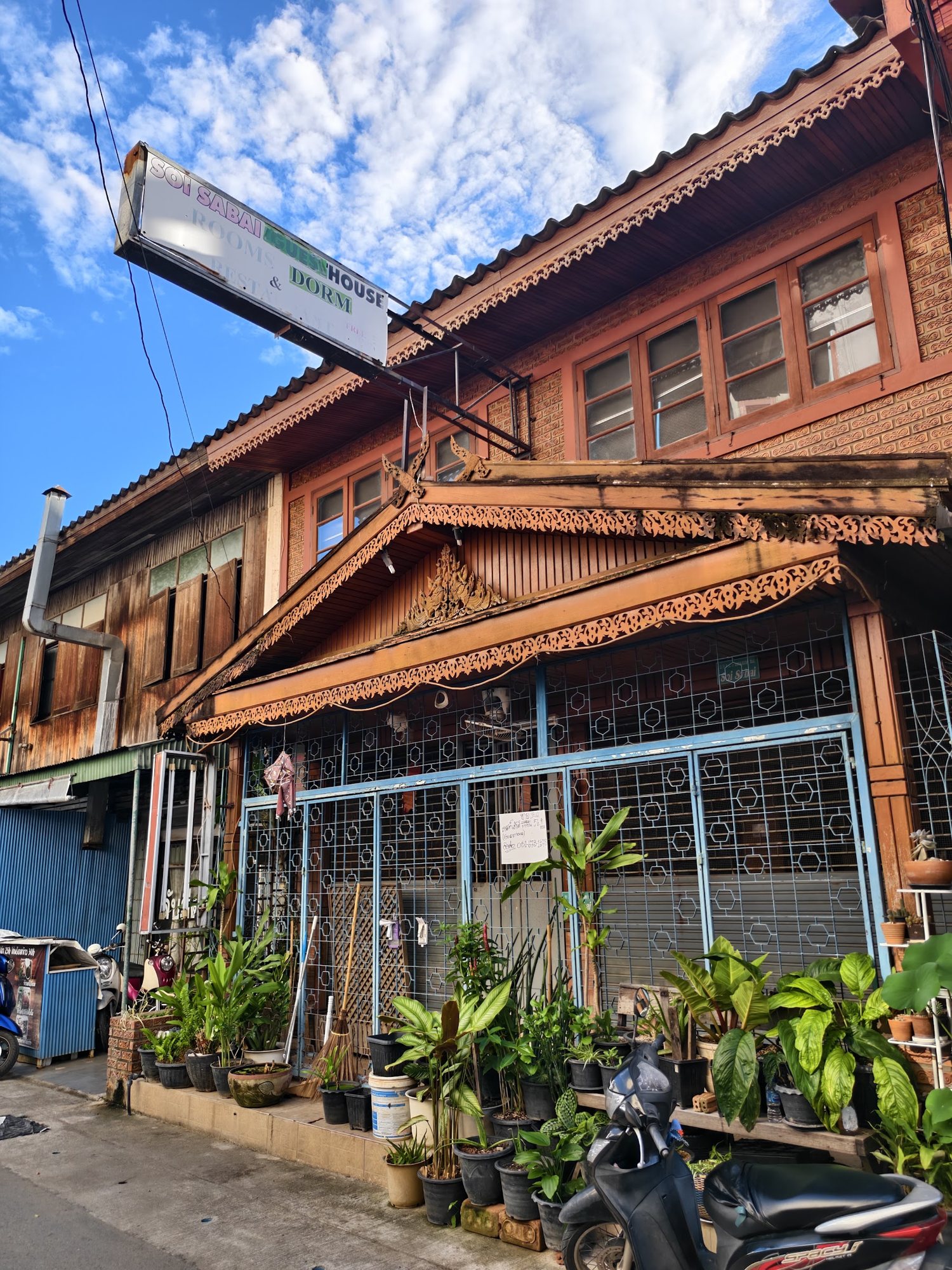 Soi Sabai Guesthouse's teak front, plants along the gate