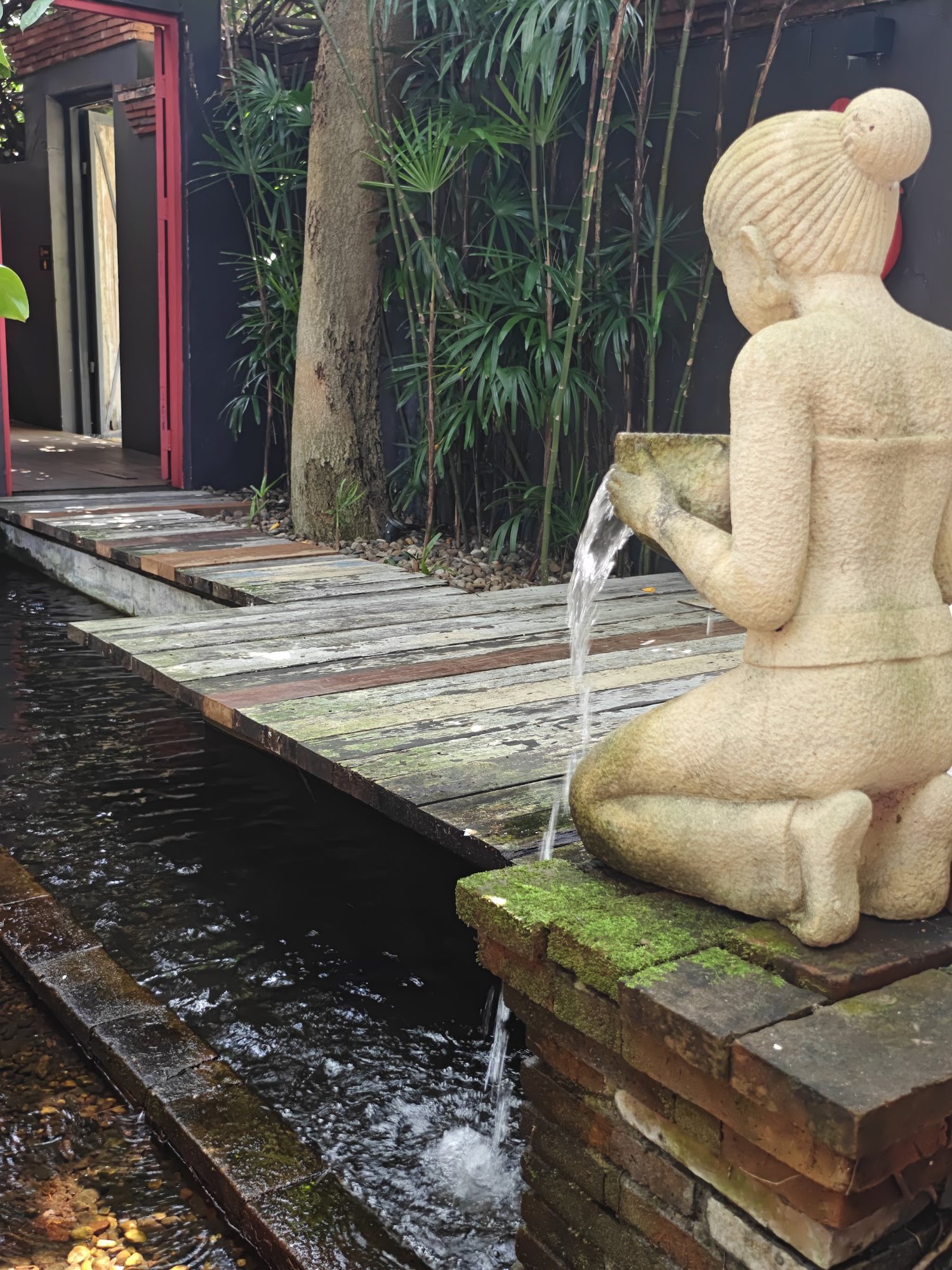 A kneeling stone figure pours water into a channel at Café de Oasis