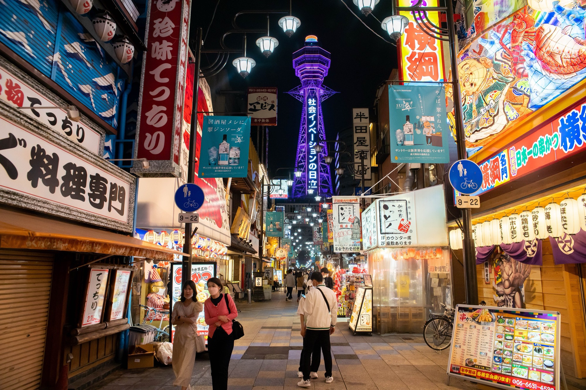 Tsutenkaku tower lit purple at the end of a lane of signs in Shinsekai, Osaka, at night