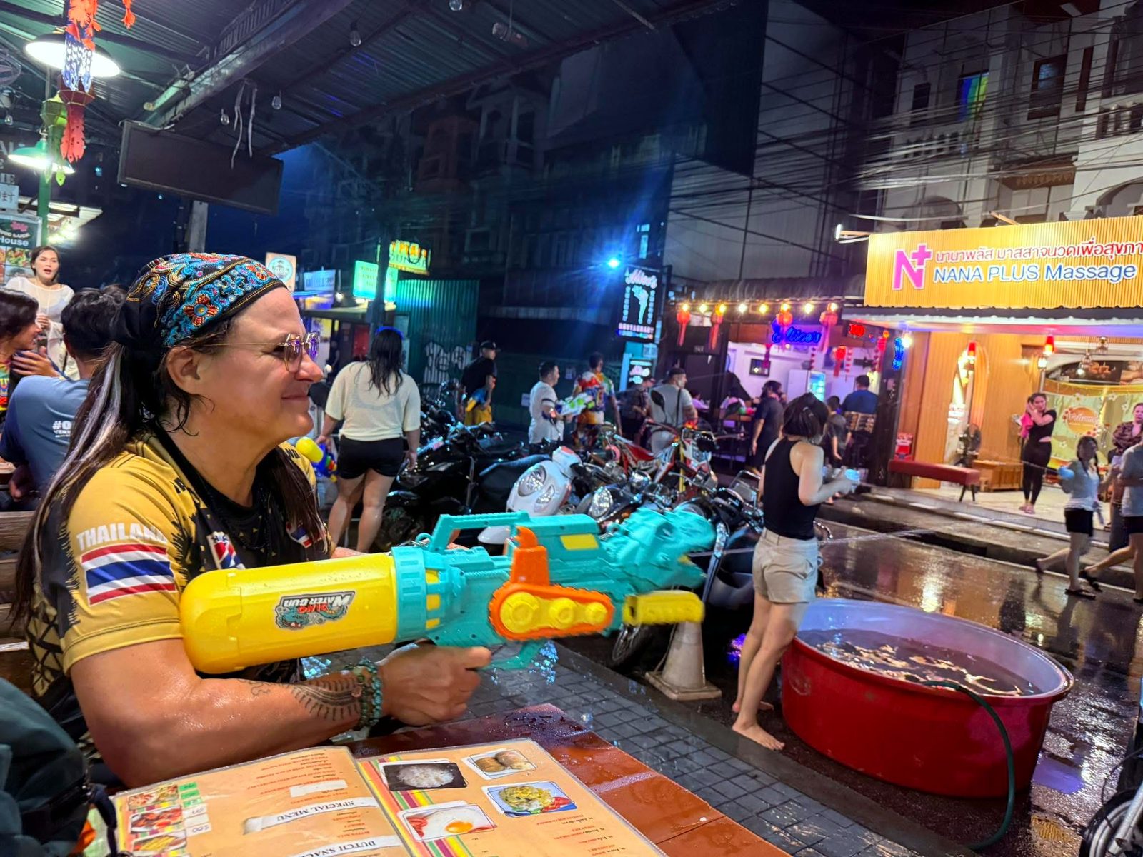 แนนกับปืนฉีดน้ำ ที่โต๊ะหน้าร้าน คืนสงกรานต์ · NaN with a water gun at a front table, Songkran night