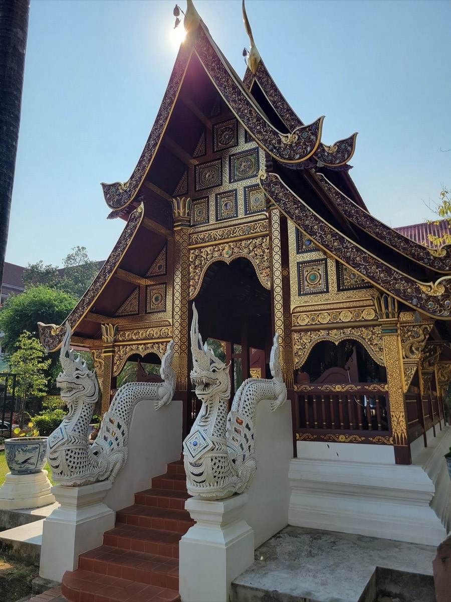 A naga coils down the entrance stair of a small viharn.