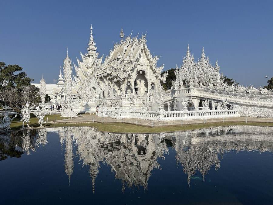 Wat Rong Khun in white relief, mirrored in its pond.