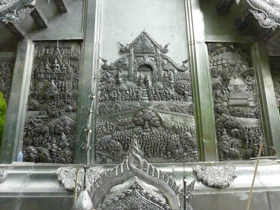 A crowded scene beaten in silver on the ubosot wall.