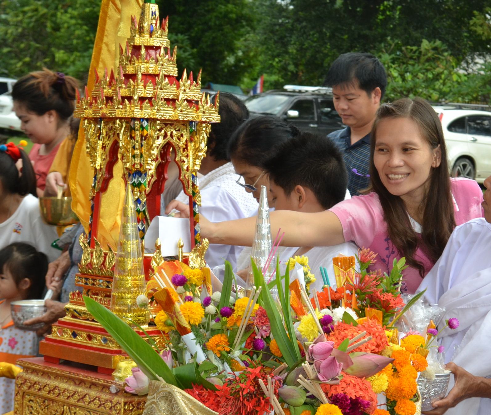 Tak Bat Devo: people place food and flowers in monks' bowls beside a gilded shrine, 2013
