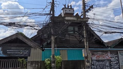 Dark-wood Lanna house behind a compound wall