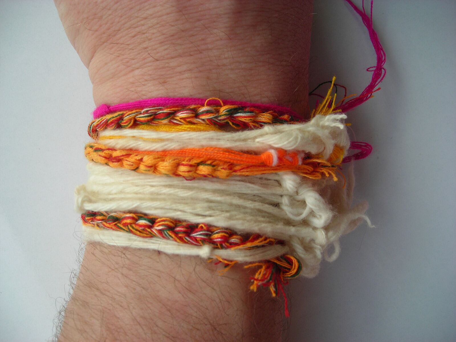 Close-up of a wrist stacked with white, orange and pink braided and knotted cotton threads.