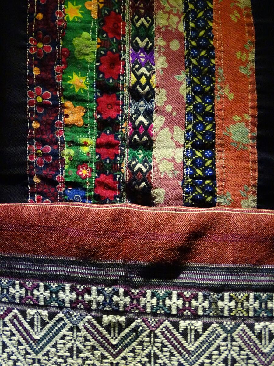 Close-up of Tai Lue woven and embroidered cloth in narrow bands of red, green, black and yellow flowers and geometric patterns.