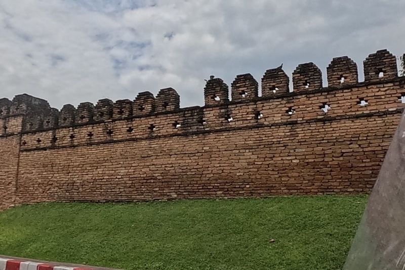 A crenellated brick city wall with a fresh lawn in front sits at a corner of the old moat.